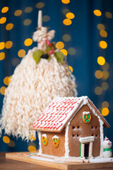 Vertical photo. National traditional Georgian Merry Christmas symbol Chichilaki and brown gingerbread house on table. Garland on blue curtain. Golden bokeh light. New Year fair, winter holiday gift