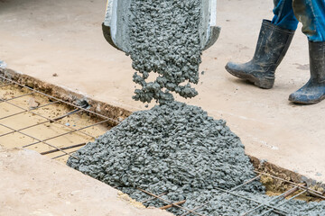 Wet concrete being poured from a yellow chute onto steel reinforcement bars at a construction site