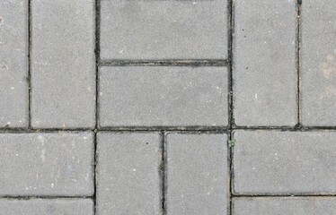 A textured cement tile floor featuring rectangular and square paving blocks arranged in a grid pattern.