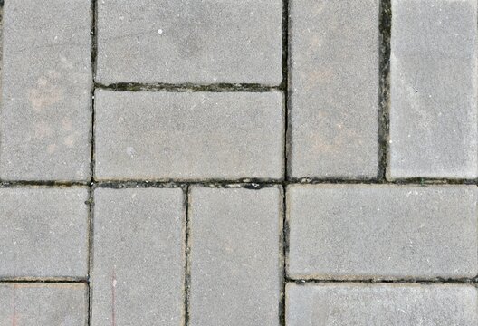 A textured cement tile floor featuring rectangular and square paving blocks arranged in a grid pattern.