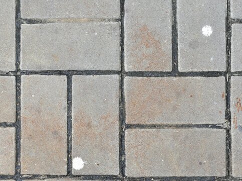 A textured cement tile floor featuring rectangular and square paving blocks arranged in a grid pattern.