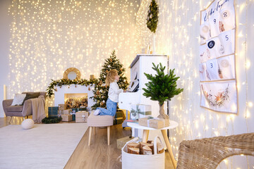 Little girl playing piano in festive room with Christmas tree and glowing string lights decoration. Child musical education during holidays.