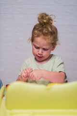 Fototapeta premium Young caucasian child with curly fair hair playing with toy. Kid with concentration at home. Learning, development, childhood concept.