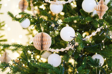 Decorated Christmas tree with white baubles and paper ornaments, twinkling lights creating a festive background for winter holiday celebration.