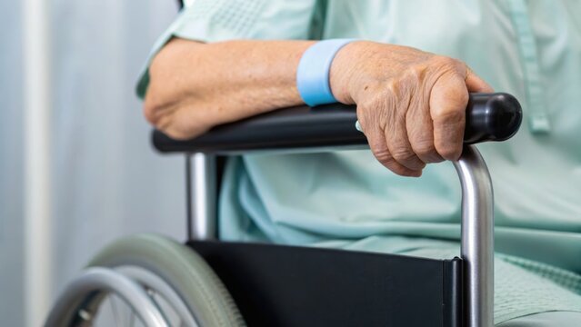 A close-up of an elderly person's hand resting on a wheelchair, conveying themes of care and mobility challenges in a healthcare setting.
