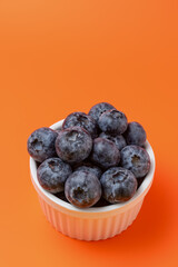 Fresh Blueberries from a White Bowl on a Vibrant Monochromatic Orange Background