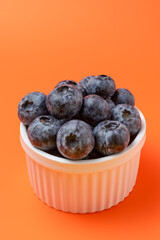 Fresh Blueberries from a White Bowl on a Vibrant Monochromatic Orange Background