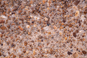 Close-up texture of small pebbles and aggregate stones embedded in a sandy surface. Rough, natural details ideal for backgrounds, construction materials, architectural textures, and design overlays.