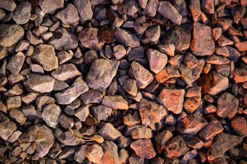 Detailed close-up texture of gravel rocks illuminated by warm sunlight. Natural stone surface ideal for backgrounds, design elements, construction themes, landscaping concepts, and abstract textures.