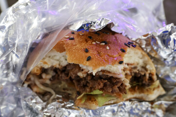 Delicious hamburger with sesame seed bun and juicy meat patty, wrapped in foil. This satisfying fast food snack makes for perfect takeout meal for quick lunch