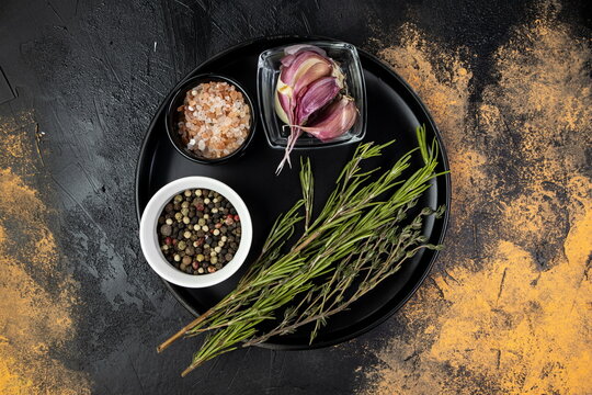 Colorful collection of fresh herbs and spices arranged on a black plate with a rustic background featuring pink salt and garlic - Powered by Adobe