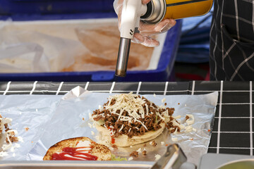 Chef using culinary torch for cooking, melting cheese over savory meat on bun. delicious food preparation process using hot flame for perfect, satisfying meal