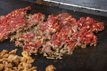 Sizzling raw red beef chopped and cooking on hot black grill. Preparation of savory meat for delicious cheesesteak or taco, creating an appetizing mouthwatering meal