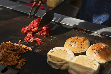 Professional chef cooking delicious street food. Sliced meat and fresh buns grilling on hot flat top griddle. mouth watering preparation for tasty burger or sandwich