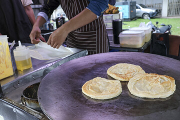 Skilled chef cooking traditional roti canai flatbread on large griddle. This focused preparation of delicious asian street food at an outdoor market shows culinary expertise
