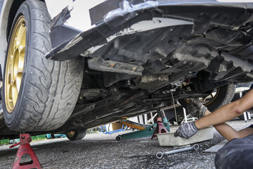 Focused auto mechanic at work on car repair and vehicle maintenance service. broken automobile undercarriage lifted on jack stand getting fixed in garage
