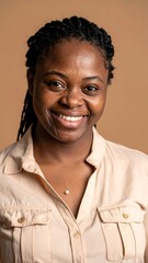 A close-up shot of a smiling Black woman with braided hair wearing a beige button-down shirt and a pearl necklace. The background is a solid tan color