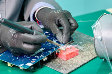 Technician soldering components on a blue circuit board in an electronics workshop during daytime hours
