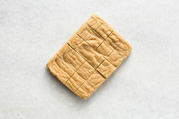 overhead view of creamy caramel fudge slab on a marble tray, sliced fudge caramel candy on white background