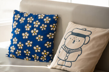 Two decorative pillows on a light-colored sofa, one with cartoon dog design and the other with a daisy floral pattern