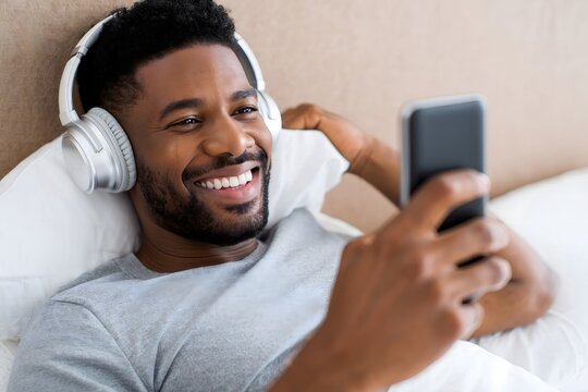 Man listening music with headphones and using mobile phone in the bed