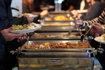 People's hands serving themselves at buffet during party or seminar in hotel, with a variety of food and drinks available.