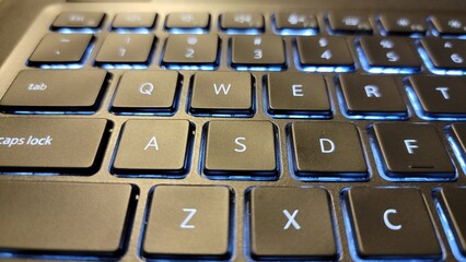 Close up of a laptop keyboard with illuminated blue backlighting visible