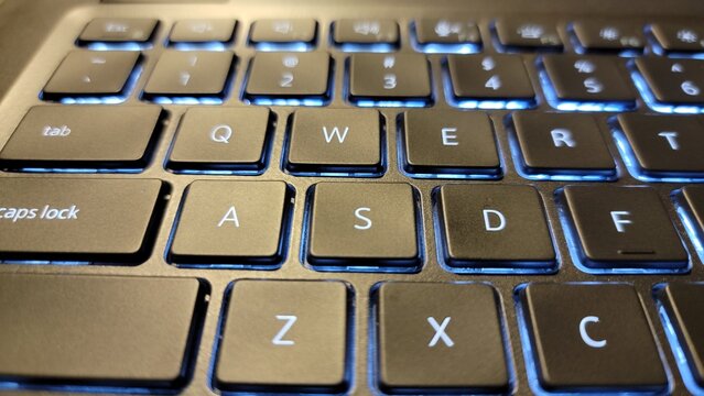 Close up of a laptop keyboard with illuminated blue backlighting visible