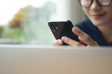 Asian business woman using smartphone, working on laptop computer at coffee shop. Freelancer online working, connecting the internet, remote work from home. Student studying online, e-learning