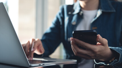 Closeup, business woman using mobile smartphone during working on laptop computer at office.
