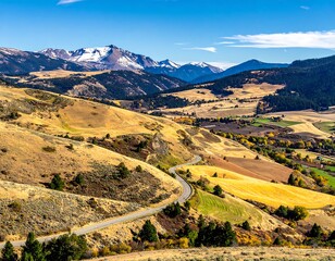 Expansive, golden fields give way to a winding road leading towards snow-capped mountain range