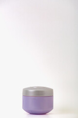 A small purple jar sits on a white background. The jar is made of plastic and has a lid. The jar is empty and he is a cosmetic product.