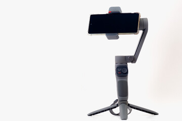 A cell phone is mounted on a tripod. The phone is black and the tripod is gray. The phone is on a white background.