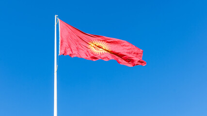 Vibrant Kyrgyzstan flag waving against a clear blue sky, showcasing intricate design elements and rich colors, symbolizing national pride and identity