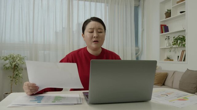 Woman gets upset while reading a document at home and crumples the paper