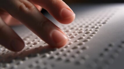 Fingers reading braille text on white paper