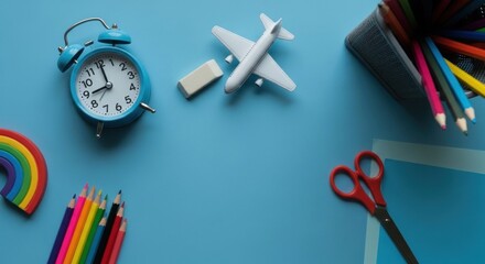 Colorful school supplies scattered on a blue surface clock, pencils, airplane, rainbow, scissors