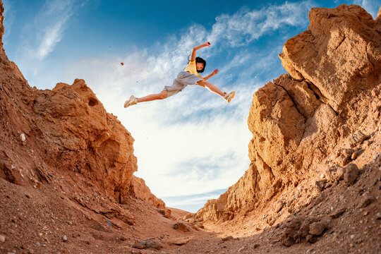 Young hiker woman girl tourist makes long jump across small gorge against blue sky - Powered by Adobe