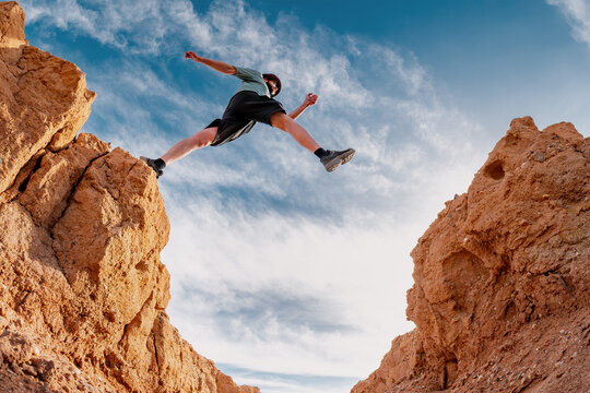 Man hiker jumps or make big step over small desert gap against blue sky