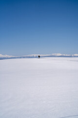 A breathtaking winter landscape of the Daisetsuzan Mountains seen from the snowy fields of Biei, Hokkaido, Japan, under a clear blue sky with untouched white snow.