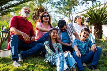 Indian family sitting on lawn slope outdoors enjoying chitchat and quality bonding time together