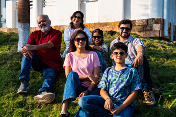Indian family sitting on lawn slope outdoors enjoying chitchat and quality bonding time together