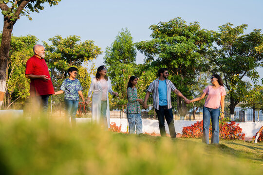 Indian family walking on lawn holding hands and enjoying happy bonding time outdoors