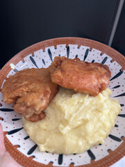 A homemade meal of crispy fried chicken thighs served with creamy mashed potatoes on a decorative plate.