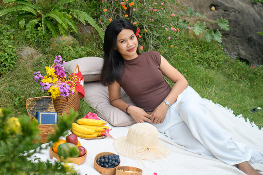 Relaxed young woman enjoying a colorful outdoor picnic in nature with fruits and flowers.