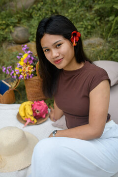 Young woman standing in a garden with a woven bag full of colorful flowers.