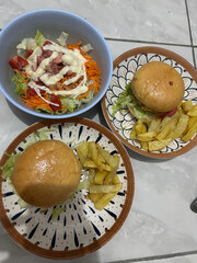 A homemade meal of two burgers with french fries and a side salad in a bowl.