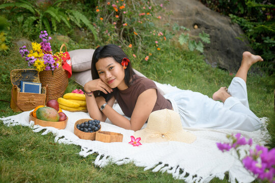 Relaxed young woman enjoying a colorful outdoor picnic in nature with fruits and flowers.