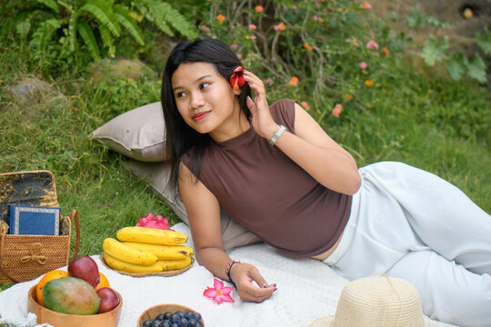 Relaxed young woman enjoying a colorful outdoor picnic in nature with fruits and flowers.