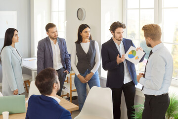 Confident business team analyzing pie chart during presentation in bright office. Male speaker explaining financial data to attentive colleagues, discussing strategies and plans for company growth.